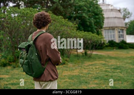 Un bel étudiant se promène dans une verdure sereine, appréciant l'air frais et la tranquillité. Banque D'Images
