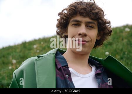 Un bel étudiant se promène dans des champs verts, rayonnant de joie et de jeunesse en plein air. Banque D'Images