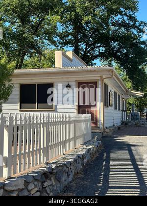 Une maison traditionnelle en bois avec une porte d'entrée rouge et une clôture blanche, entourée d'arbres dans une petite ville californienne. Banque D'Images