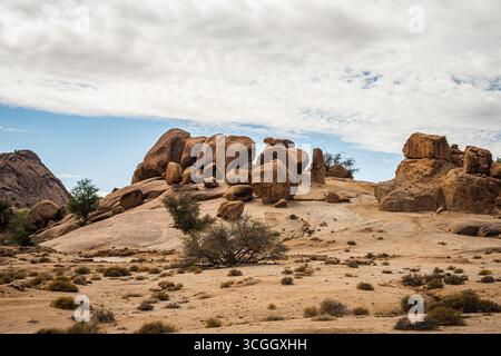 Formations rocheuses granitiques massives dans le désert de Tafraout Maroc avec végétation clairsemée, ciel spectaculaire et paysage montagneux anti-Atlas accidenté Banque D'Images