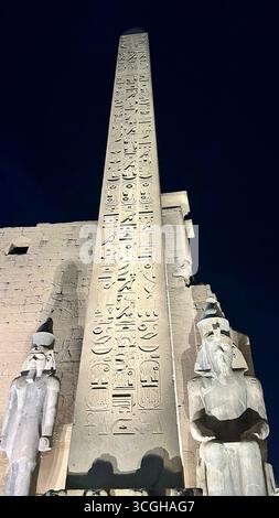Louxor, Égypte - 9 février 2025 : vue nocturne de l'obélisque illuminé et des statues colossales au pylône d'entrée du temple de Louxor en Égypte, avec hiéroglyphe Banque D'Images