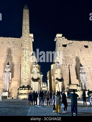 Louxor, Égypte - 9 février 2025 : entrée illuminée du temple de Louxor la nuit avec des statues colossales et un obélisque debout, avec des visiteurs dans le premier groupe Banque D'Images