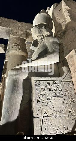 Louxor, Égypte - 9 février 2025 : statue colossale illuminée de Ramsès II au temple de Louxor avec des reliefs hiéroglyphiques sculptés sur le trône, vus la nuit f Banque D'Images