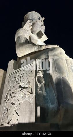 Louxor, Égypte - 9 février 2025 : statue colossale illuminée de Ramsès II au temple de Louxor avec des reliefs hiéroglyphiques sculptés sur le trône, vus la nuit f Banque D'Images