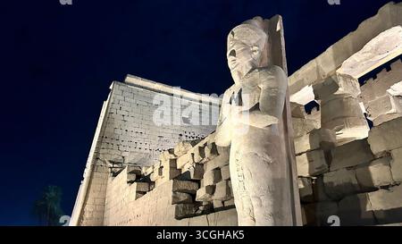 Louxor, Égypte - 9 février 2025 : vue nocturne de la statue colossale illuminée du pharaon Ramsès II à l'entrée du temple de Louxor en Égypte. Banque D'Images