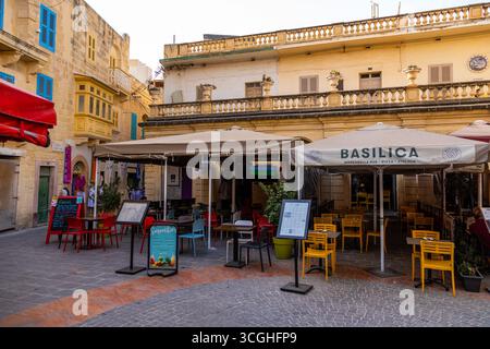 Gozo, Malte – 23 juin 2021 : image éditoriale d'un café en plein air avec des chaises colorées, des parasols et une architecture en pierre. Banque D'Images