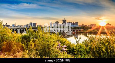 Pont enjambe une rivière avec une ville en arrière-plan. Le soleil se couche, projetant une lueur chaude sur la scène Banque D'Images