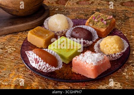 Bonbons indiens assortis sur plaque décorative, disposés dans des gobelets en papier. Plat traditionnel mithai posé sur la surface dorée pour la photographie culinaire festive. 🔍 Al Banque D'Images