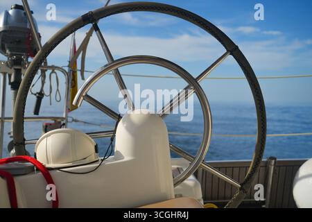 Gros plan d'une barre de yacht en acier inoxydable avec casque de sécurité et corde rouge sur le pont, mer bleue calme et ciel en arrière-plan. Banque D'Images
