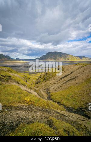 Vaste paysage montagneux islandais avec des collines couvertes de mousse, des rivières tressées et des montagnes volcaniques lointaines sous un ciel spectaculaire Banque D'Images