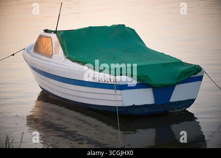 Barca blanca con franja azul y toldo verde, fueraborda sin Motor puesto y anclado en la orilla del rio odiel frente a las tres carabelas en Palos F.. Banque D'Images