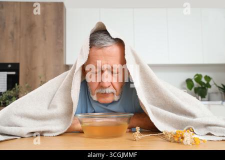 Homme mûr avec serviette faisant inhalation de vapeur à table dans la cuisine Banque D'Images