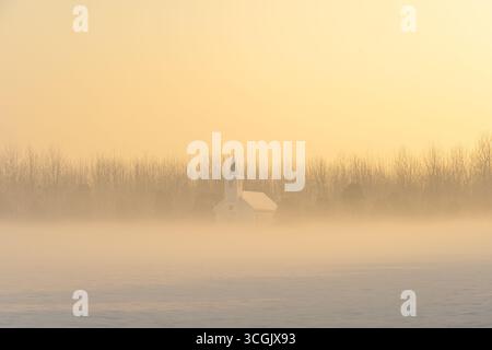 Un petit bâtiment blanc se dresse dans un paysage brumeux sous un ciel jaune doux. Banque D'Images