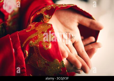 Détail de mariage chinois : mariée tenant anneau de fiançailles dans la manche brodée rouge Banque D'Images