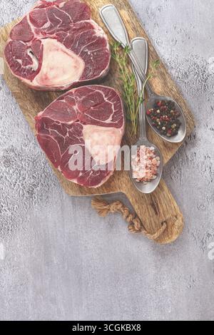 Cuisses de bœuf fraîchement tranchées, deux steaks ossobuco, sur une planche de bois, avec des épices et des herbes, prêtes à cuire Banque D'Images