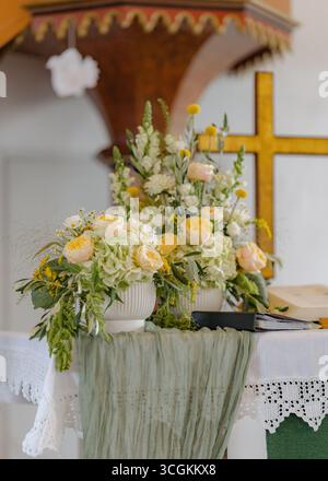 Un bel arrangement floral avec des roses et des hortensias décore un autel d'église, complété par un drapé de tissu. La configuration comprend une croix et ouverte Banque D'Images