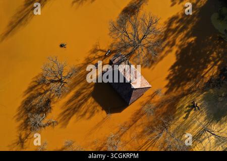 Vue aérienne de la maison de village en train de couler au milieu de l'étang de décantation de drainage de mine acide toxique. Geamana, Rosia Montana, Roumanie Banque D'Images