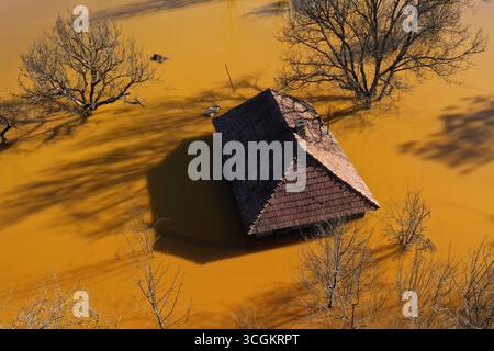 Vue aérienne de la maison de village en train de couler au milieu du lac de décantation de mines toxiques Banque D'Images