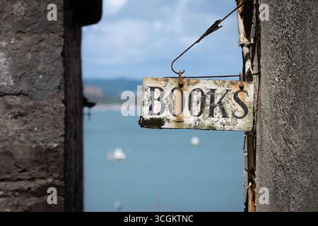 Une vieille enseigne, des livres publicitaires, accrochée à un mur de magasin, surplombant un littoral idylique Banque D'Images