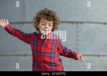 Enfant en chemise à carreaux rouge jouant avec les bras tendus Banque D'Images