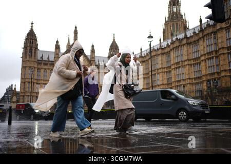 Les femmes s'abritent de la pluie dans des manteaux imperméables alors qu'elles traversent Westminster, le centre de Londres, pendant une averse. Date de la photo : vendredi 29 août 2025. Banque D'Images