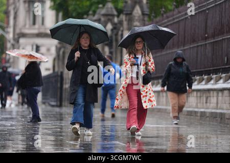 Les femmes s'abritent de la pluie sous des parapluies alors qu'elles traversent Westminster, le centre de Londres, pendant une averse. Date de la photo : vendredi 29 août 2025. Banque D'Images