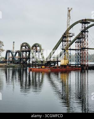 Pont piétonnier en construction. Chantier de construction d'un pont suspendu en voûte sur la rivière. Les structures métalliques du pont inachevé se reflètent dans l'eau. Banque D'Images