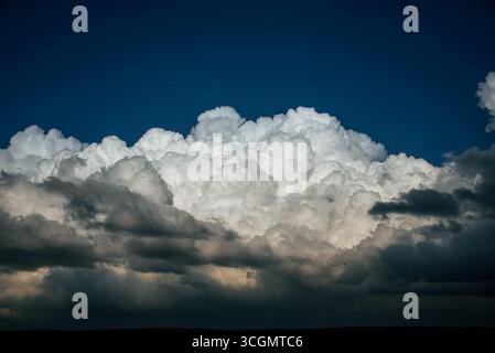 Des nuages de cumulus blancs brillants se forment au-dessus d'un paysage sombre, créant un contraste spectaculaire avec le ciel bleu profond, laissant entendre une tempête qui approche Banque D'Images