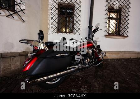 Rzeszow, Pologne - 22 août 2025 : une moto Yamaha XVS 1300 Midnight Star polie à côté d'un bâtiment dans le quartier historique de Rzeszow la nuit. Banque D'Images