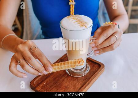 Femme savourant un délicieux latte tout en tenant une gaufrette croustillante dans un cadre de café confortable Banque D'Images