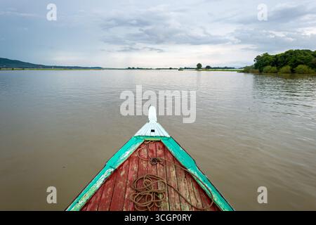 Ayeyarwaddy River from Wooden Bow Mandalay // MANDALAY, Myanmar — la proue d'un bateau fluvial traditionnel en bois navigue sur la rivière Ayeyarwady (également connue sous le nom de rivière Irrawaddy) près de Mandalay. Cette importante voie navigable est la plus longue rivière du Myanmar, coulant environ 2 170 kilomètres (1 350 miles) du nord au sud. Il sert de voie de transport vitale et de ligne de vie économique pour le pays, reliant diverses régions. Mandalay, la deuxième plus grande ville du Myanmar, est un centre économique et culturel majeur situé sur la rive est de l'Ayeyarwady. La rivière est centrale à la vie quotidienne et Li Banque D'Images