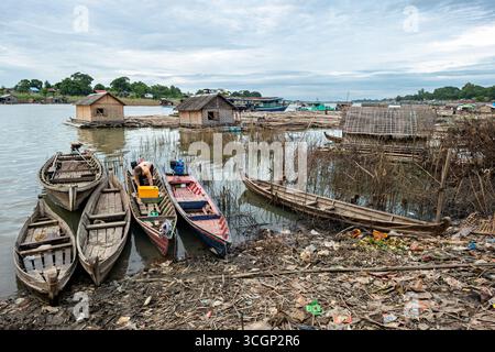 Quais du fleuve Ayeyarwaddy Bateaux Maisons flottantes et pollution Mandalay Myanmar | MANDALAY, Myanmar — Des bateaux à rames en bois et des maisons flottantes au toit de chaume encombrent les quais du fleuve Ayeyarwaddy, avec des déchets plastiques et des bois flottés entassés le long de la rive. Les communautés riveraines vivent ici sur ou à côté de l'eau, un modèle d'établissement façonné par les crues saisonnières du fleuve et par la pollution croissante en plastique et agricole documentée sur son bassin de 156 000 miles carrés (404 200 km carrés). Banque D'Images
