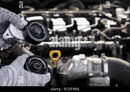 Auto Mechanic maintient la tension et la poulie folle pour la courroie multi-gorges d'agrégat d'entraînement. Concept de réparation et d'entretien de voiture, générateur, direction assistée, et pompe à vide, règlements Banque D'Images
