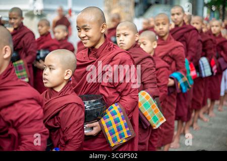 Monastère de Mahagandayon Young Buddhist novices Lunch Line Mandalay Myanmar // MANDALAY, Myanmar — de jeunes novices bouddhistes s’alignent pour déjeuner au monastère de Mahagandayon. Ce rituel quotidien est une partie fondamentale de la vie monastique, où des centaines de moines et de novices reçoivent leurs repas. Le monastère de Mahagandayon (également connu sous le nom de monastère de Mahagandayone) est l'un des collèges monastiques les plus grands et les plus respectés au Myanmar. Situé à Amarapura, un canton de Mandalay, c'est un centre important pour l'éducation bouddhiste et un site important pour les visiteurs. Le monastère joue un rôle crucial dans la préservation de Therav Banque D'Images