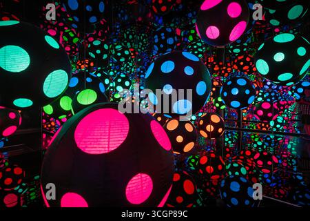 Musée Hirshhorn et jardin de sculptures Yayoi Kusama Infinity Room Washington DC | WASHINGTON DC — des sphères à pois bleues, vertes, roses et oranges sont suspendues à l’intérieur d’une chambre en miroir dans cette salle Yayoi Kusama Infinity Room au musée Hirshhorn et jardin de sculptures, avec un visiteur légèrement visible sur le bord droit des reflets. L'installation appartient à la longue série Infinity Mirrored Room de Kusama, qui utilise des lumières et des miroirs pour suggérer un espace sans limite. Banque D'Images