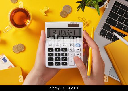 Mains tenant calculatrice avec budget mot à l'écran. Argent, ordinateur portable et papeterie jaune. Finance et concept d'entreprise avec copyspace. Banque D'Images