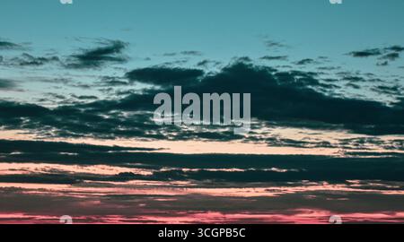 Le ciel brille d'enchantement pendant le coucher du soleil, où les couleurs pastel et les nuages doux peignent une vision rêveuse du soir. Banque D'Images