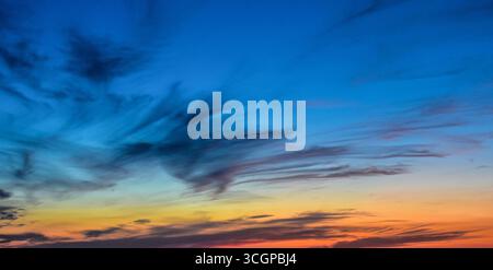 Scène crépusculaire époustouflante avec des nuages pastel éclairés par le coucher de soleil caché, projetant un charme doux et brillant sur le ciel. Banque D'Images