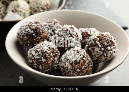 Délicieux bonbons au chocolat avec des noix et des flocons de noix de coco dans un bol sur la table, gros plan Banque D'Images