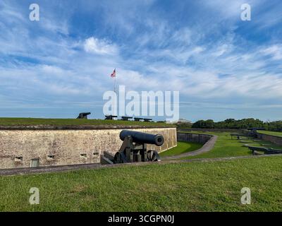 Rangée de canons historiques positionnés le long des remparts herbeux du Fort Macon State Park en Caroline du Nord, avec le drapeau américain flottant fièrement au-dessus. Banque D'Images