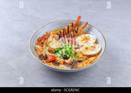 Gros plan d'authentiques ramen japonais avec tempura de crevettes frites croustillantes, œuf dur, oignons verts, champignons, tomates, et des nouilles dans un riche bouillon, servi moi Banque D'Images