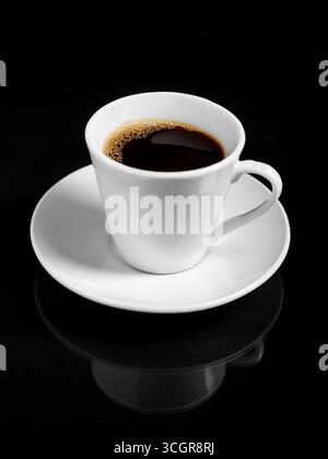 Une tasse de café torréfié noir fumant repose sur une soucoupe blanche sur un fond noir. Banque D'Images