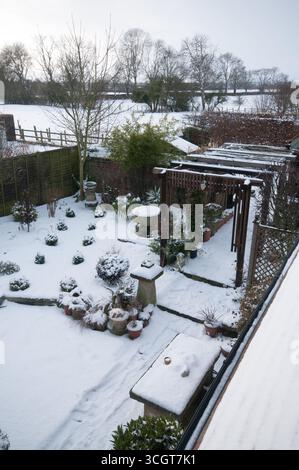 Un jardin d'hiver serein recouvert de neige, avec des chemins soigneusement conçus et des parterres de fleurs magnifiquement disposés sous un ciel nuageux. Banque D'Images
