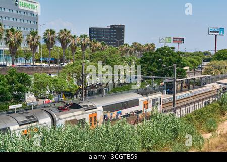 Viladecans. Barcelone - 29 août 2025 : un train Rodalies de Catalunya avec graffitis entre dans la gare de Viladecans, dans un paysage urbain avec des hôtels Banque D'Images