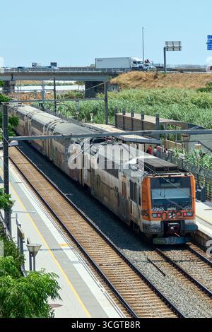 Viladecans. Barcelone - 29 août 2025 : un train de voyageurs à la gare, encadré par la végétation et les infrastructures autoroutières, illustrant conn de banlieue Banque D'Images