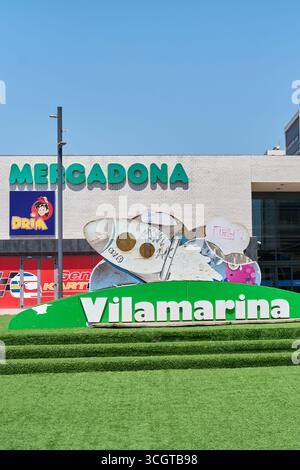 Viladecans. Barcelone - 29 août 2025 : le design moderne de l'espace public du centre commercial, avec gazon artificiel et sculpture, accueille la visite Banque D'Images