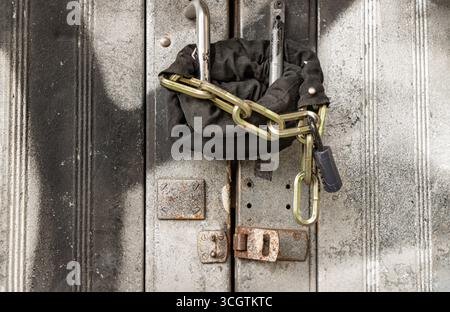 une porte métallique qui est en effet verrouillée à l'aide d'une chaîne robuste enroulée autour des poignées et sécurisée avec un cadenas. une mesure de sécurité pour un entrepôt, Banque D'Images
