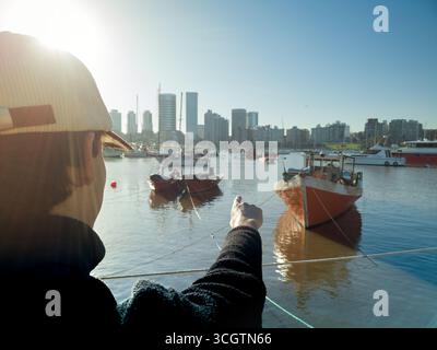 Pêcheur amarrage bateau dans un port avec une ligne d'horizon de la ville en arrière-plan, par une journée ensoleillée Banque D'Images