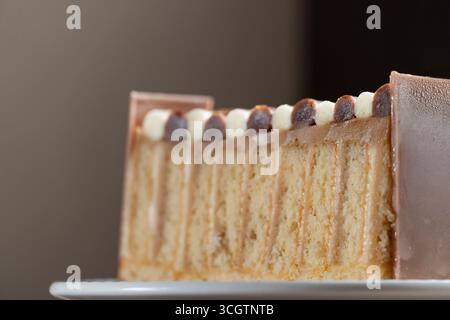Gros plan d'une tranche de gâteau superposée avec une garniture crémeuse, recouverte d'une alternance de boules de chocolat blanc et noir, et enveloppée d'une couche de chocolat lisse Banque D'Images
