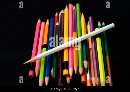 Une variété de crayons de couleur sont empilés de manière artistique, avec des teintes vives sur un fond sombre, mettant en valeur une atmosphère accueillante pour Banque D'Images